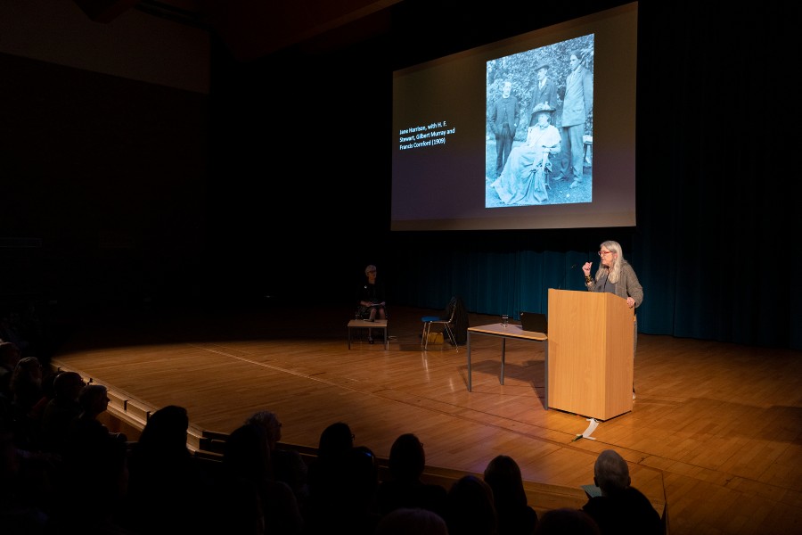 A woman stands on a stage in front of a screen showing a black and white photograph